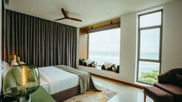 A bedroom with a large bed, a view of the ocean, a panda-themed window seat, and a ceiling fan.