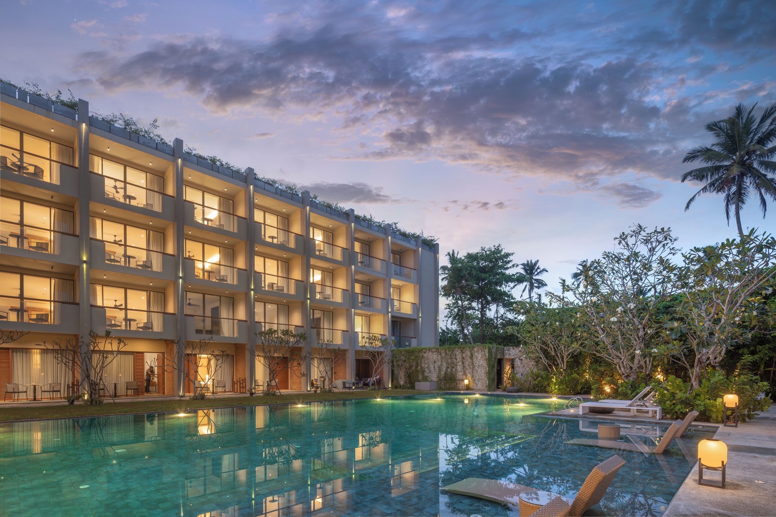A hotel with a large outdoor swimming pool, multiple balconies, and lush greenery.