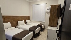 Habitación de hotel con tres camas, un refrigerador pequeño, televisor y ventana con persiana.