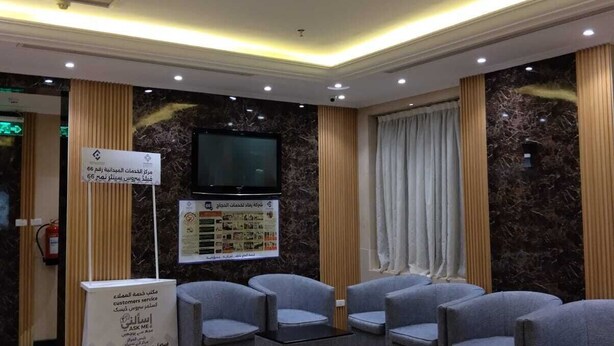 Vestíbulo de hotel con zonas de estar, mostrador de recepción, televisor y carteles informativos.