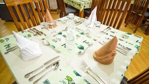 Une table à manger dressée avec des couverts, des verres et des serviettes, recouverte d’une nappe ornée d’un motif de feuilles vertes.
