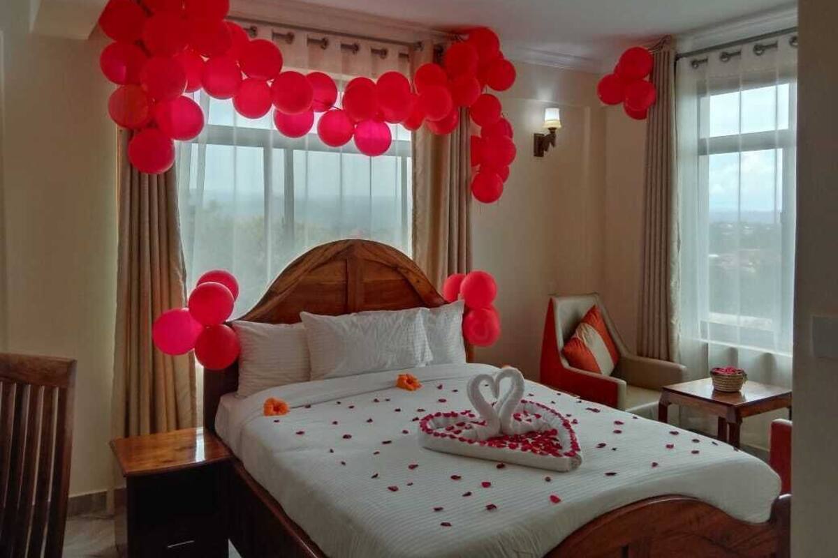 A hotel room with a large bed, a wooden headboard, and red balloons.