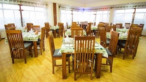 Un espace repas comprenant plusieurs tables et chaises, disposées dans une pièce spacieuse dotée de grandes fenêtres.