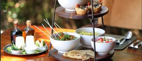 A three-tiered serving tray with various dishes and a bottle of olive oil on a wooden table.
