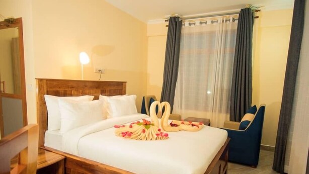 Une chambre d’hôtel avec un lit en bois, du linge de lit blanc, un miroir, une table de chevet et un fauteuil bleu.