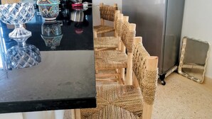 Een keuken met een roestvrijstalen koelkast, een zwart aanrecht en rieten stoelen.