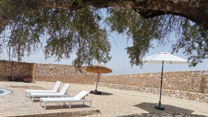 Een zonnig buitenzitgedeelte met witte loungestoelen en een achtergrond van een stenen muur.