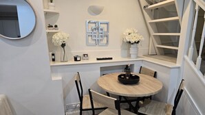 Un comedor con una mesa redonda de madera, sillas negras y un jarrón blanco con flores.