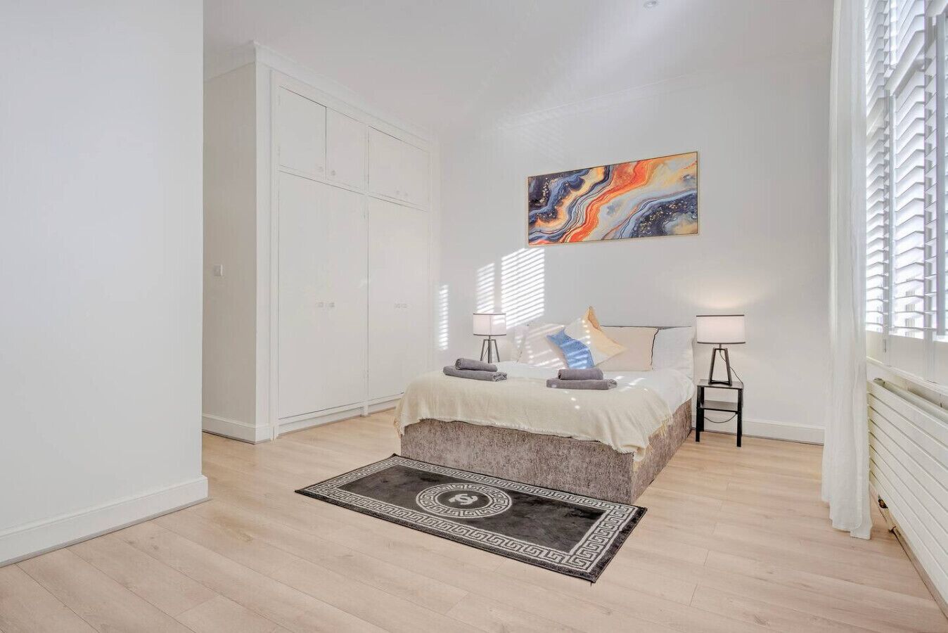 A bedroom with a bed, bedside lamps, a rug, and a painting on the wall.