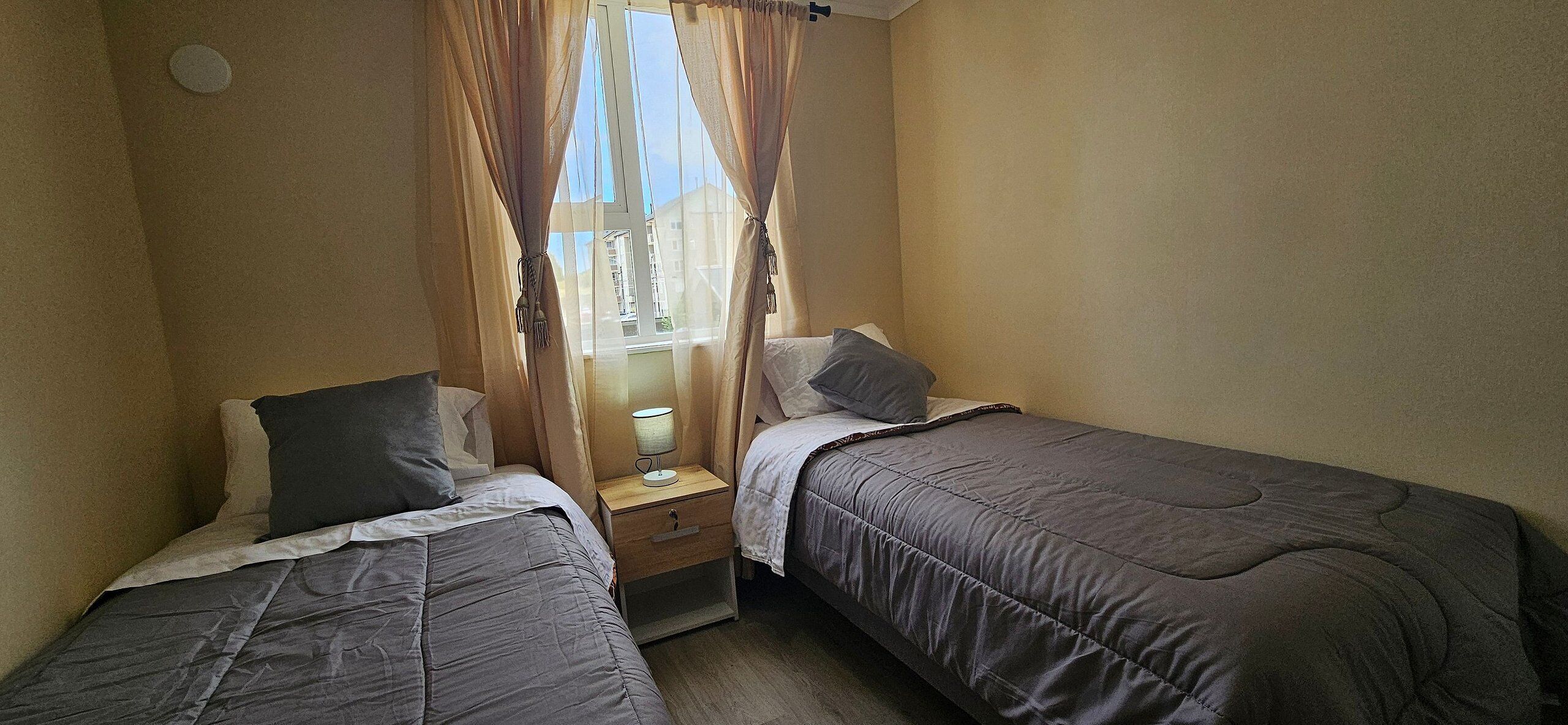 A bedroom with two single beds, a nightstand with a lamp, and a window with curtains.