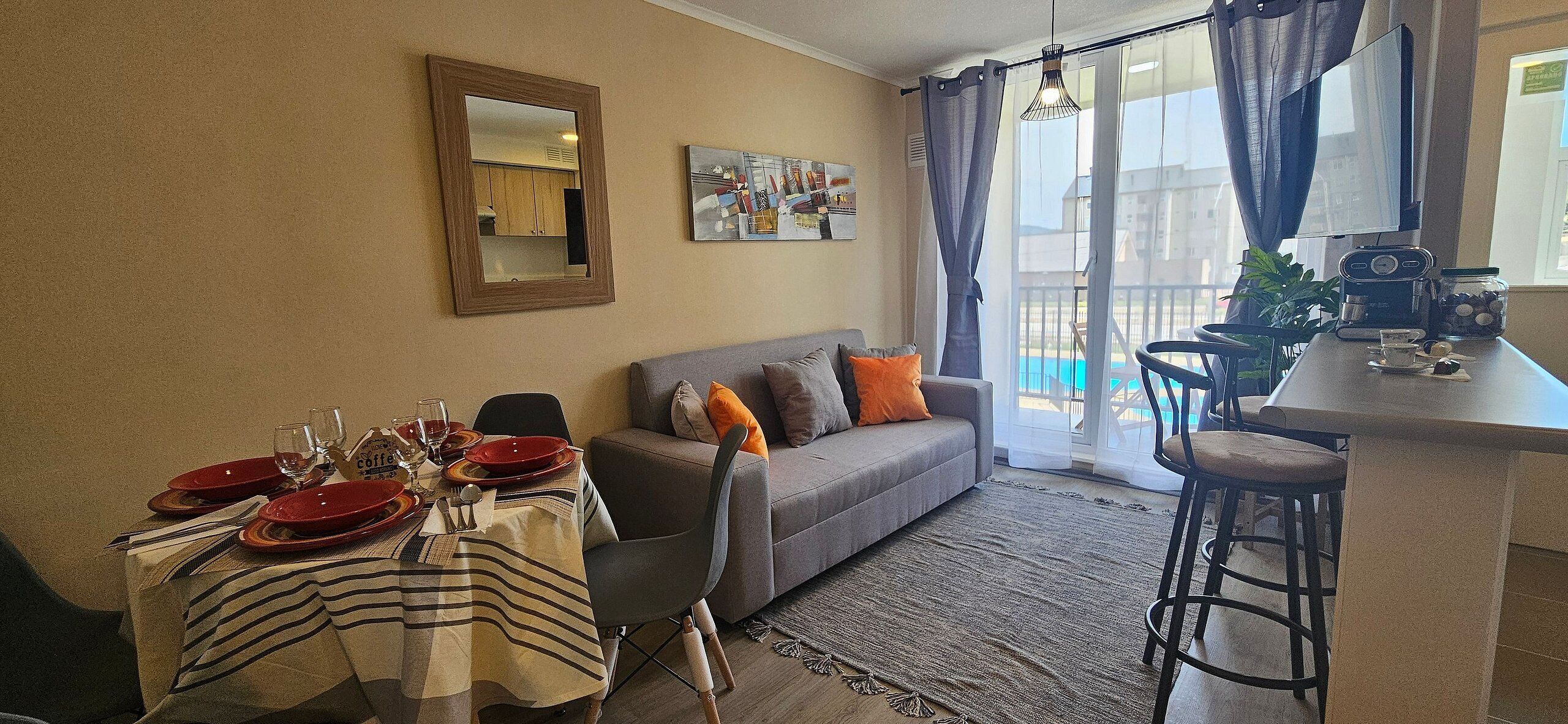 A living room with a sofa, dining table set, and a kitchen area with a coffee machine.