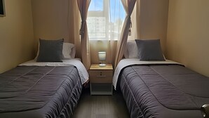 Une chambre double avec deux lits, une table de chevet avec une lampe et une fenêtre avec des rideaux.