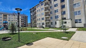 Un immeuble résidentiel doté de nombreux balcons, d’un terrain de jeux avec un toboggan et d’une pelouse bien entretenue.
