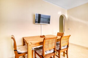 Un coin repas avec une table et des chaises en bois, un téléviseur à écran plat fixé au mur et un sol carrelé.