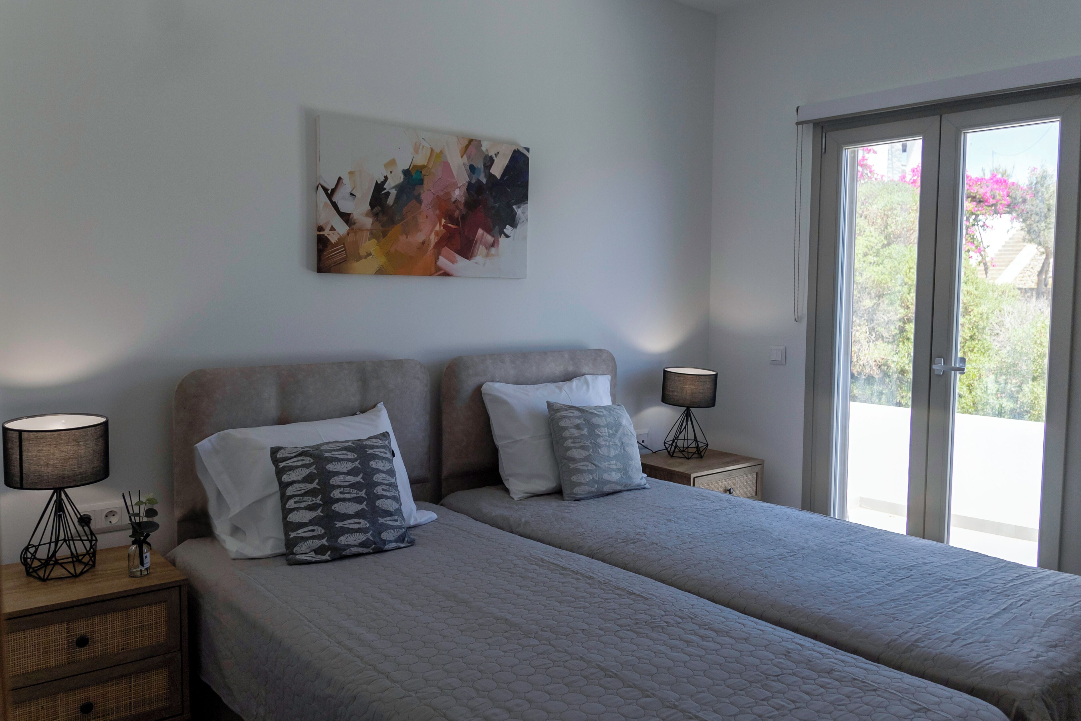 Ein Schlafzimmer mit zwei Betten, einem großen abstrakten Gemälde und Blick durch das Fenster.