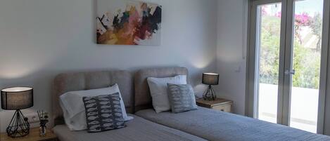 Ein Schlafzimmer mit zwei Betten, einem großen abstrakten Gemälde und Blick durch das Fenster.