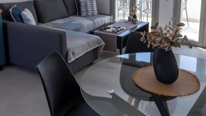 Una sala de estar moderna con una mesa de comedor de vidrio, un sofá gris y una obra de arte en la pared.