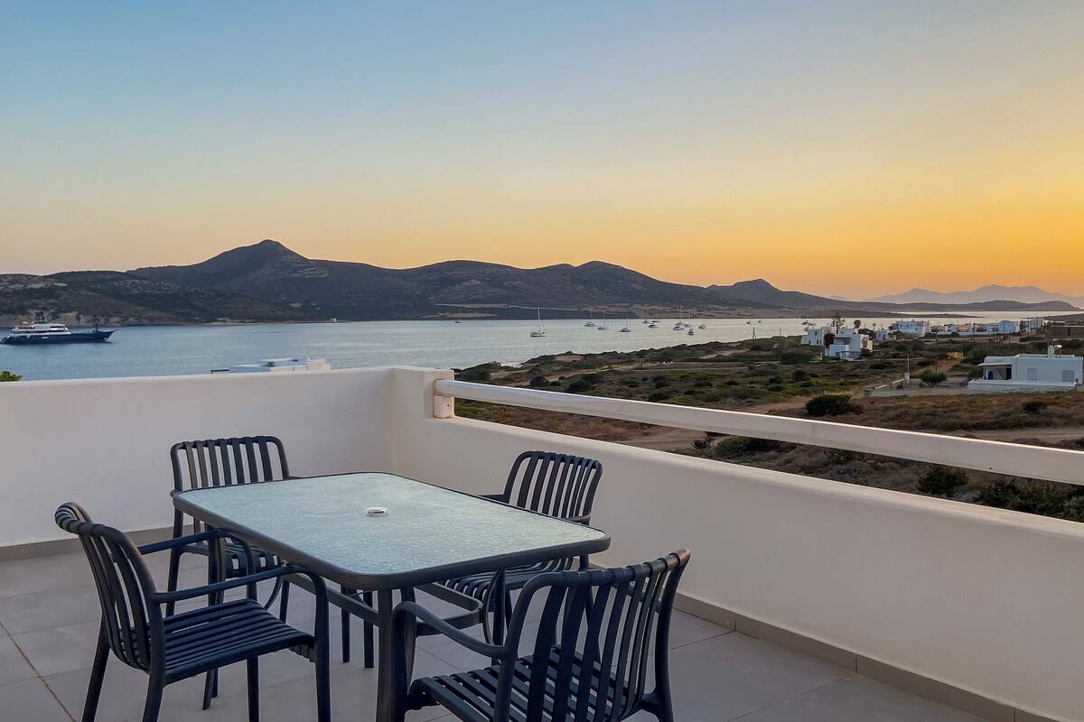 Une terrasse avec une table et des chaises donnant sur une zone côtière, avec des bateaux et des bâtiments.