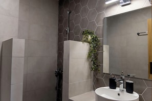 A modern bathroom with a white sink, black soap dispensers, a mirror, and a shower with a hexagonal tile pattern.