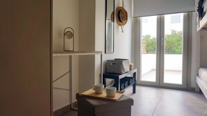 Una habitación moderna con puerta de vidrio corrediza que da a un balcón, una mesita con dos tazas, un espejo y un sombrero colgado en la pared.