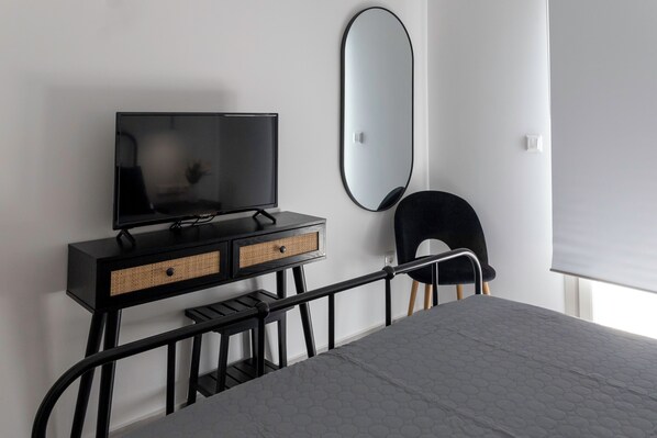 Une chambre à coucher avec un lit, un téléviseur posé sur une commode noire, une chaise et un grand miroir accroché au mur.