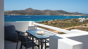 Un balcón con mesa y sillas que da a un paisaje costero con montañas y el mar.