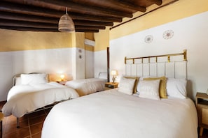 Quarto de hotel com duas camas, vigas de madeira no teto, ar condicionado fixado na parede e uma luminária de cabeceira.