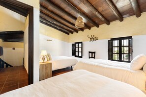 Una habitación con dos camas, vigas de madera en el techo, una lámpara colgante y una ventana con contraventanas.