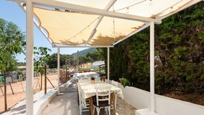 An outdoor patio with a table and chairs, a canopy, and a view of a mountainous landscape.