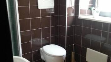 Un baño con inodoro, lavamanos y bidé. Hay estantes con artículos de aseo y un espejo sobre el lavamanos.
