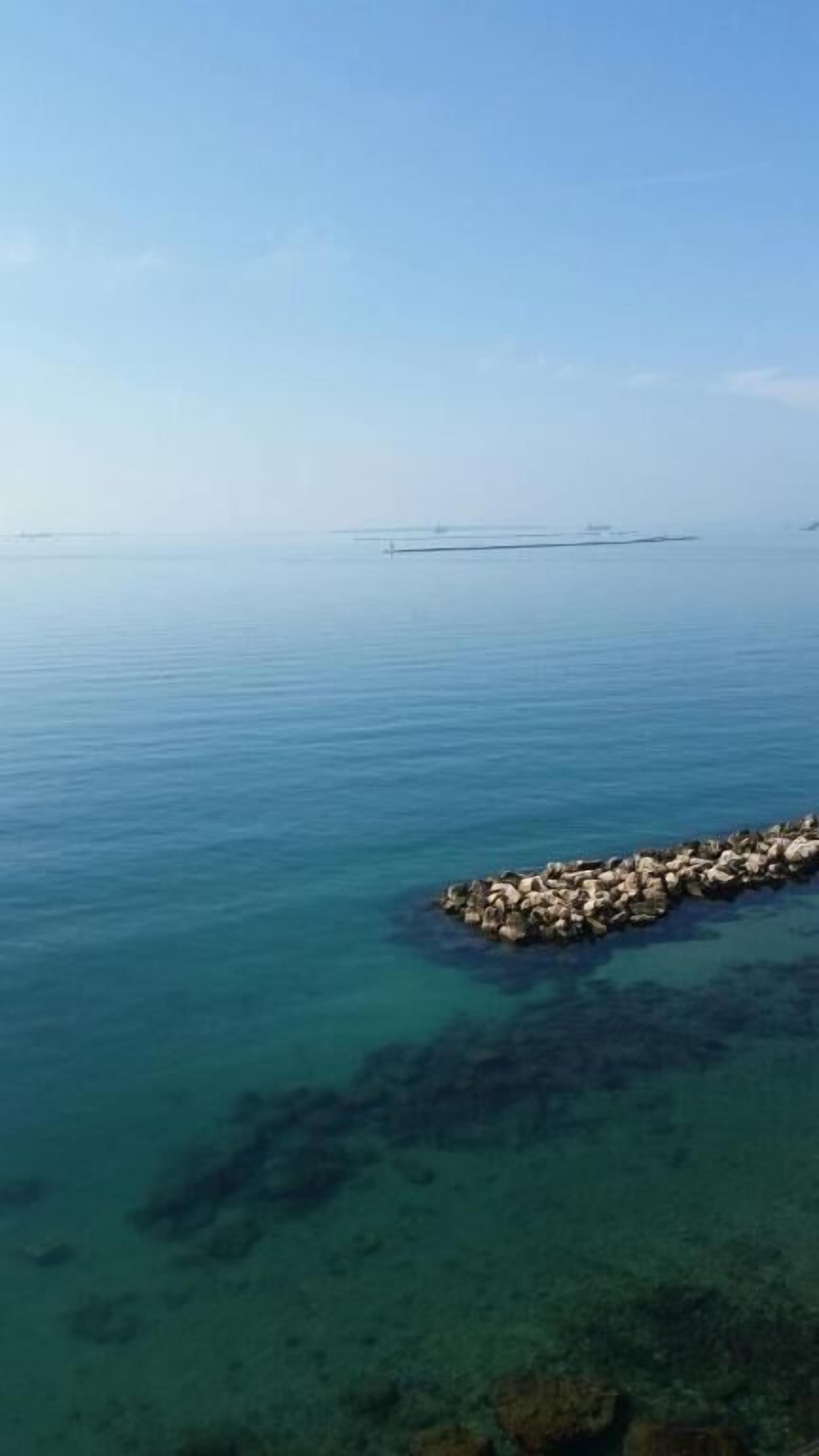 Ein freier Blick auf ruhiges Meer mit einem steinernen Wellenbrecher im Vordergrund.