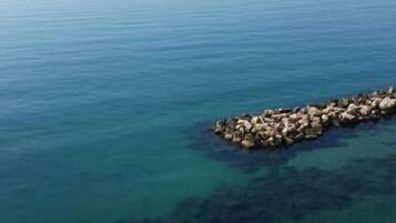A clear view of a calm sea with a rocky breakwater in the foreground.