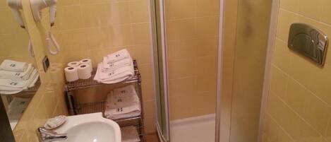 Un baño con lavamanos, inodoro y ducha. Se observan toallas y artículos de aseo.