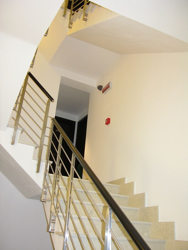 A staircase with metal railings and beige steps, leading to a landing with a red fire alarm. - baja delle sirene (Taranto)