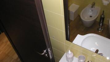 A bathroom with a mirror, sink, bidet, and a bottle of hand soap.