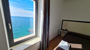 A bedroom with a large window offering a view of the sea, a bed with a headboard, a nightstand, and a lamp. - baja delle sirene (Taranto)