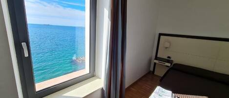Un dormitorio con un ventanal grande que ofrece vistas al mar, una cama con cabecera, una mesita de noche y una lámpara.