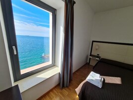 Un dormitorio con un ventanal grande que ofrece vistas al mar, una cama con cabecera, una mesita de noche y una lámpara.