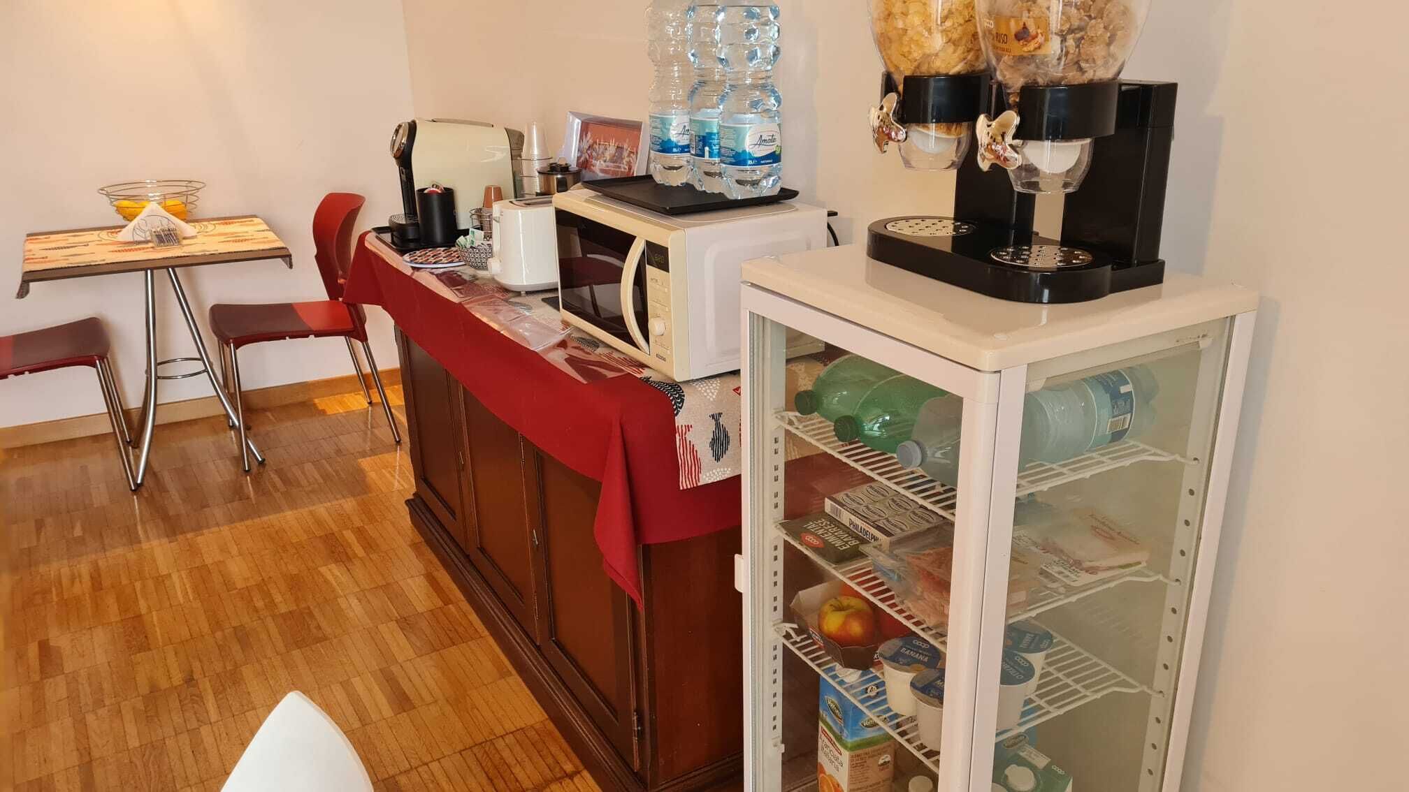Una cucina compatta con forno a microonde, macchina del caffè e distributore d'acqua. Un frigorifero pieno di viveri.