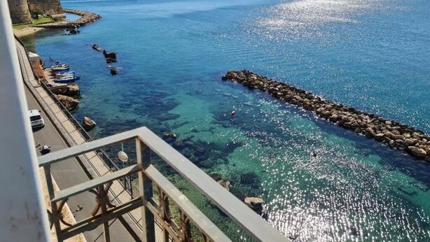A coastal view with a clear blue sea, a rocky breakwater, and a cityscape in the background. - baja delle sirene (Taranto)