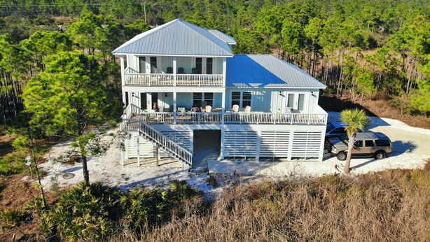 Una casa sulla spiaggia a due piani con un balcone, un portico coperto e una scalinata che conduce all'ingresso.