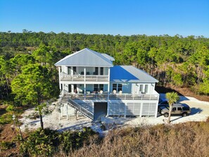 A two-story beach house with a balcony, a covered porch, and a staircase leading to the entrance. - In Morgantown - Pools & Pickleball! (Gulf Shores)
