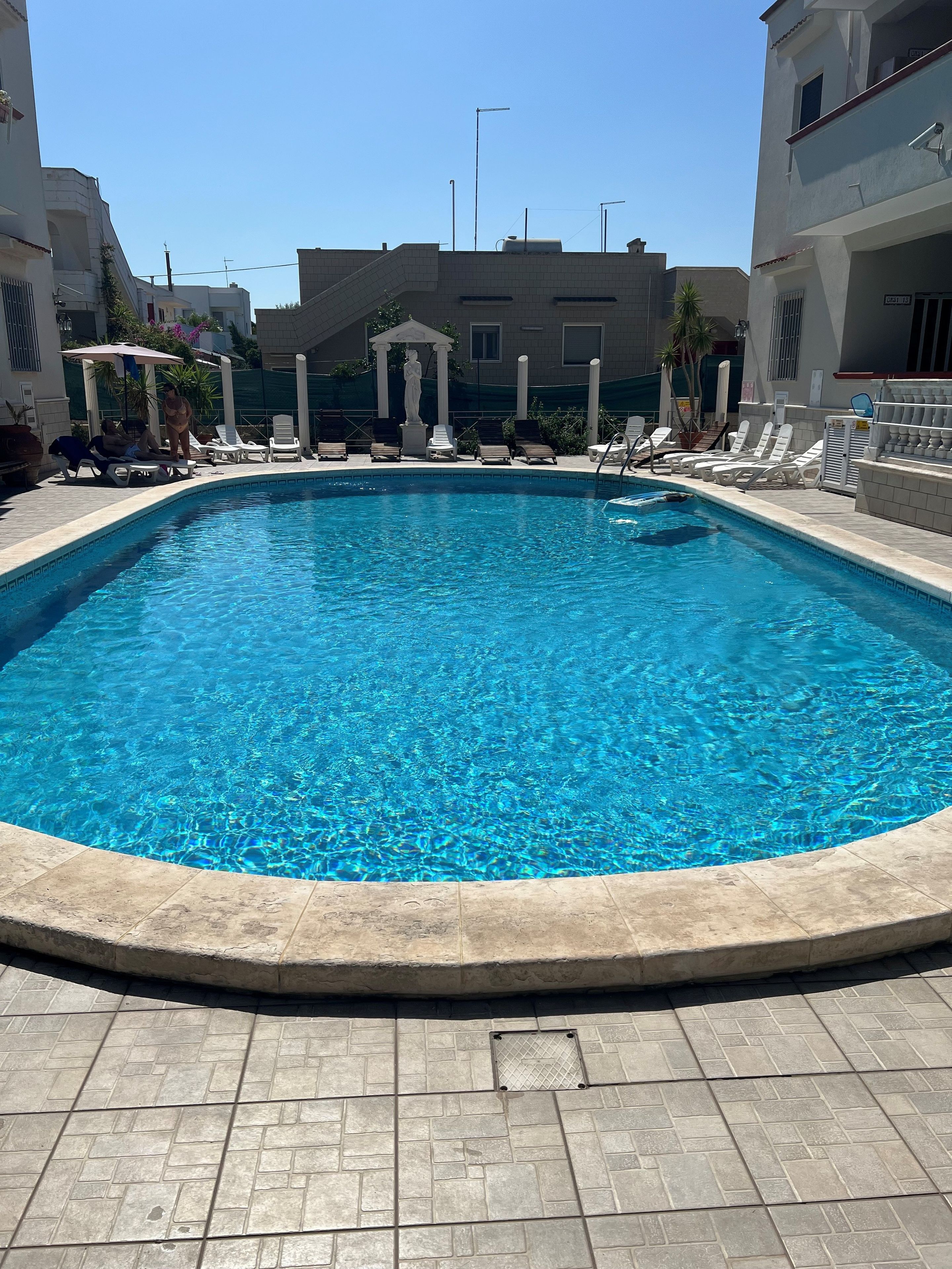 A swimming pool with lounge chairs and a statue, surrounded by buildings.