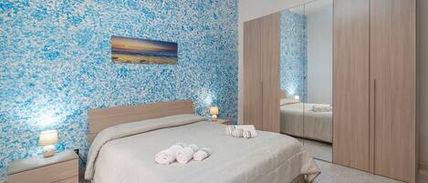 Un dormitorio con cama, mesitas de noche, un espejo y una pared con estampado floral.
