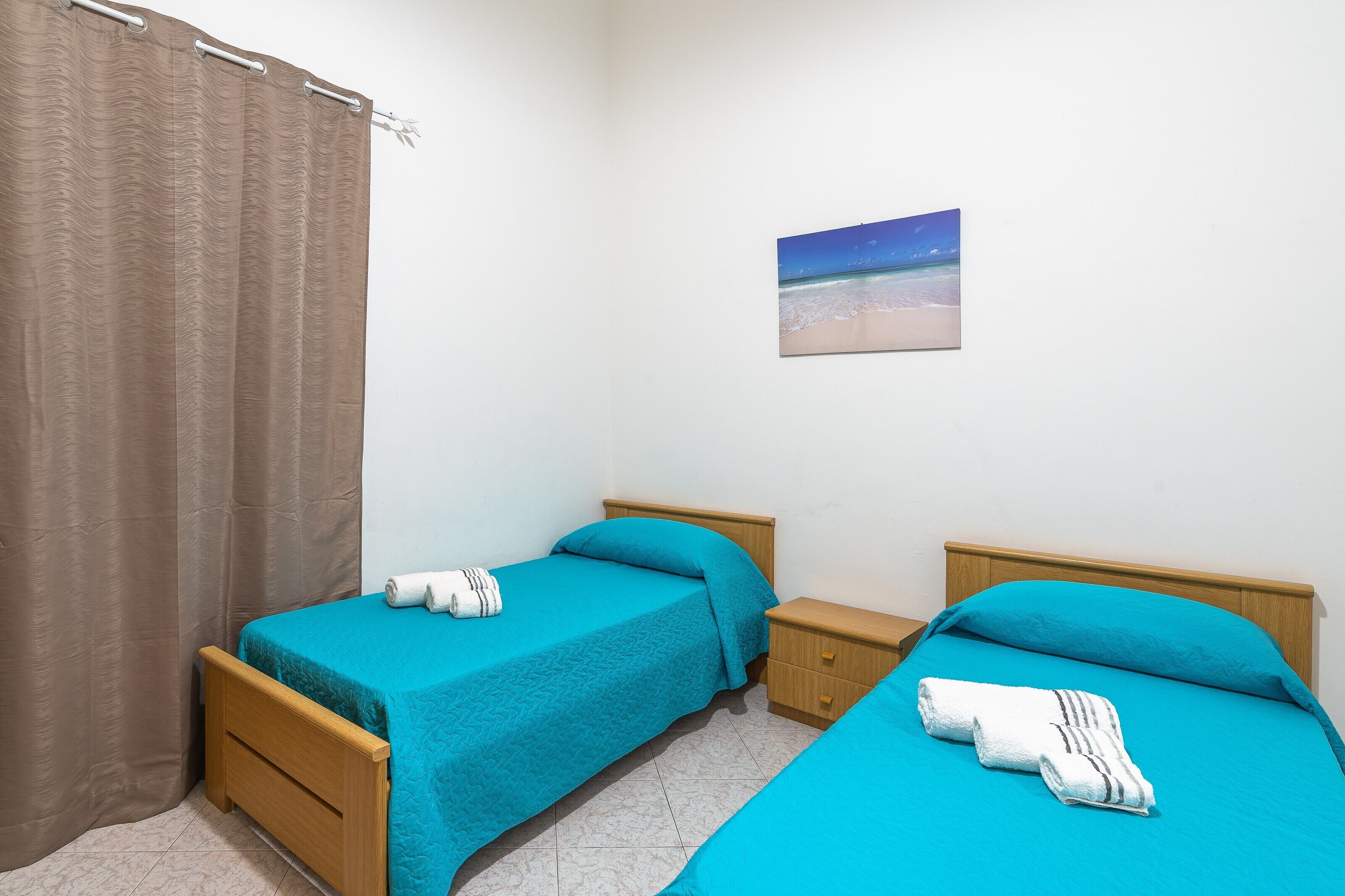 Una camera da letto con due letti singoli, un comodino, una tenda da bagno e un quadro con vista sulla spiaggia.