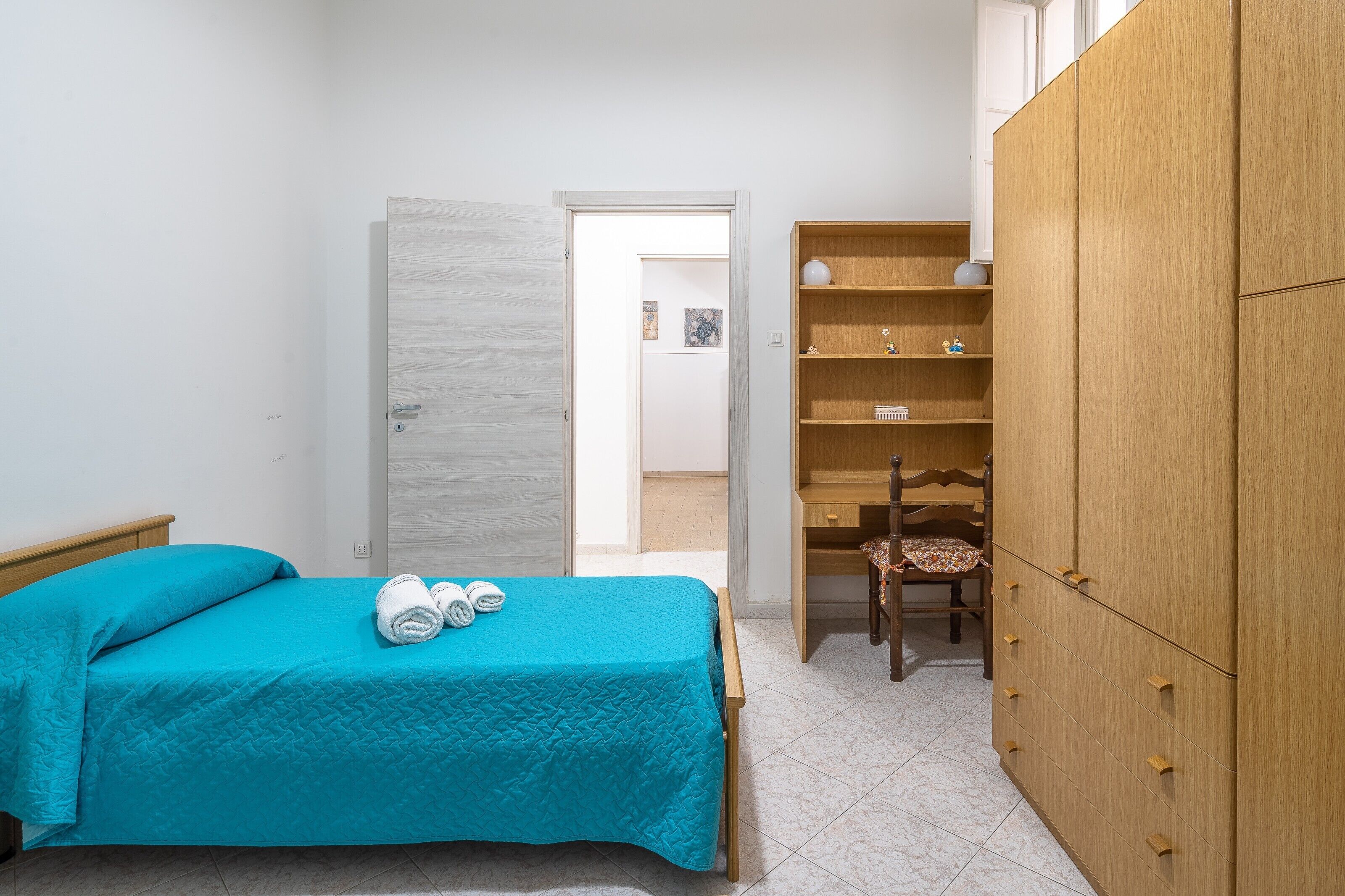 Un dormitorio con cama, armario, silla y puerta que da a otra habitación.