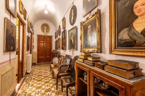 A hallway with framed portraits, a bust sculpture, and a wooden cabinet with books.