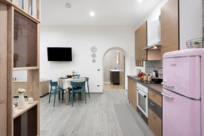 A modern kitchen with a pink refrigerator, wooden cabinets, and a dining area with teal chairs.