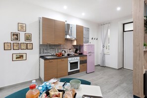 A modern kitchen with wooden cabinets, a stainless steel range hood, a pink refrigerator, and a dining area with a table set for two.
