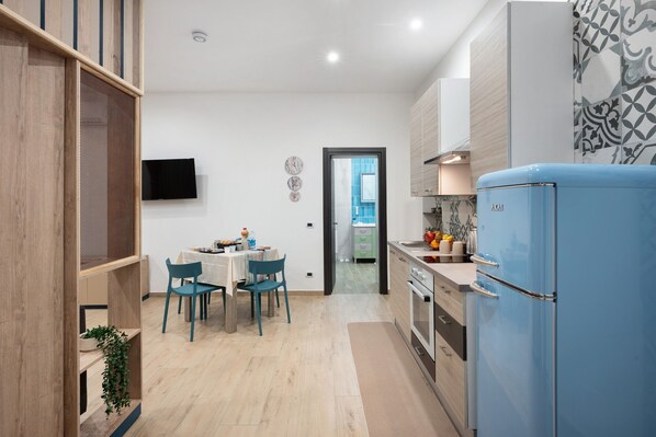 A modern kitchen with a blue refrigerator, wooden cabinets, and a dining area with chairs and a table.